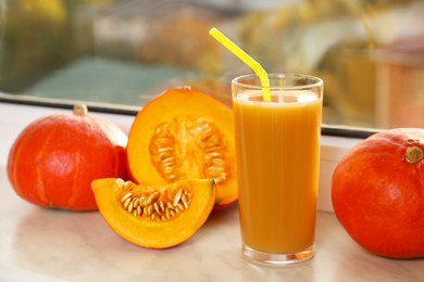 Photo of Tasty pumpkin juice in glass, whole and cut pumpkins on windowsill indoors