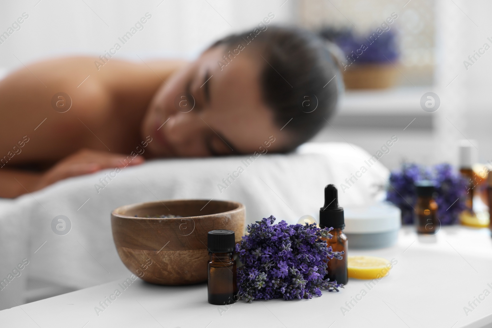 Photo of Woman relaxing on massage couch and bottles of essential oil with ingredients on table in spa salon, selective focus