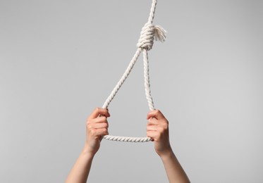 Photo of Woman holding rope noose on light grey background, closeup