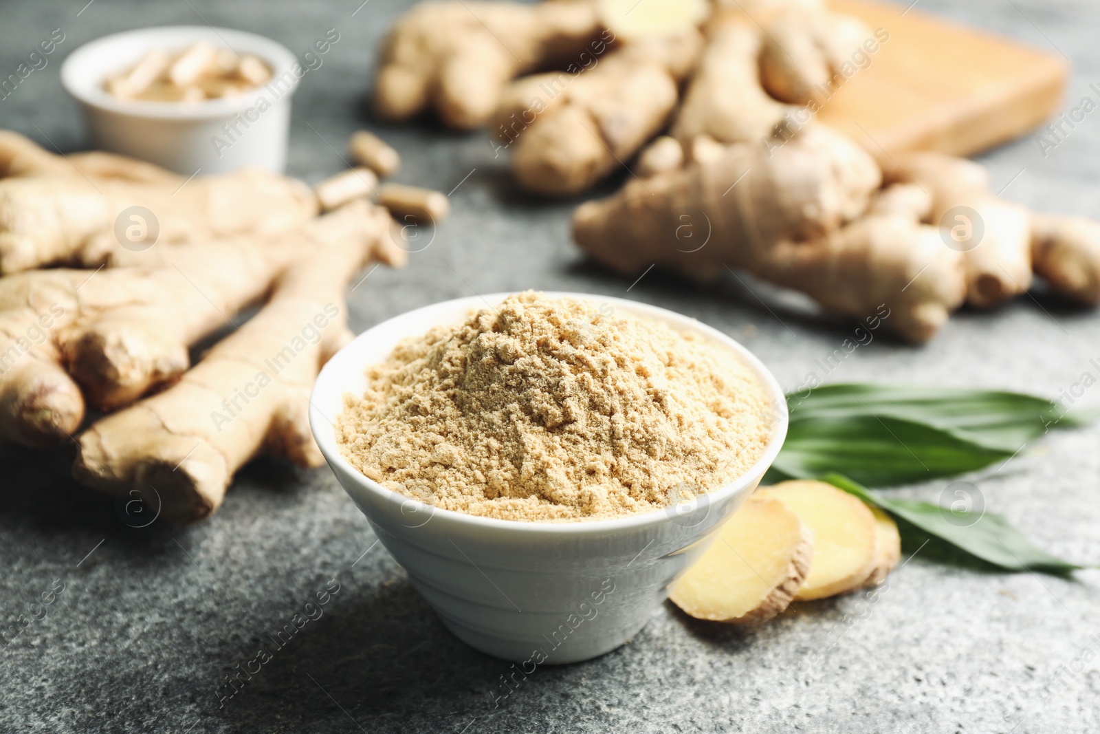 Photo of Dry ginger powder, fresh root and leaves on grey table