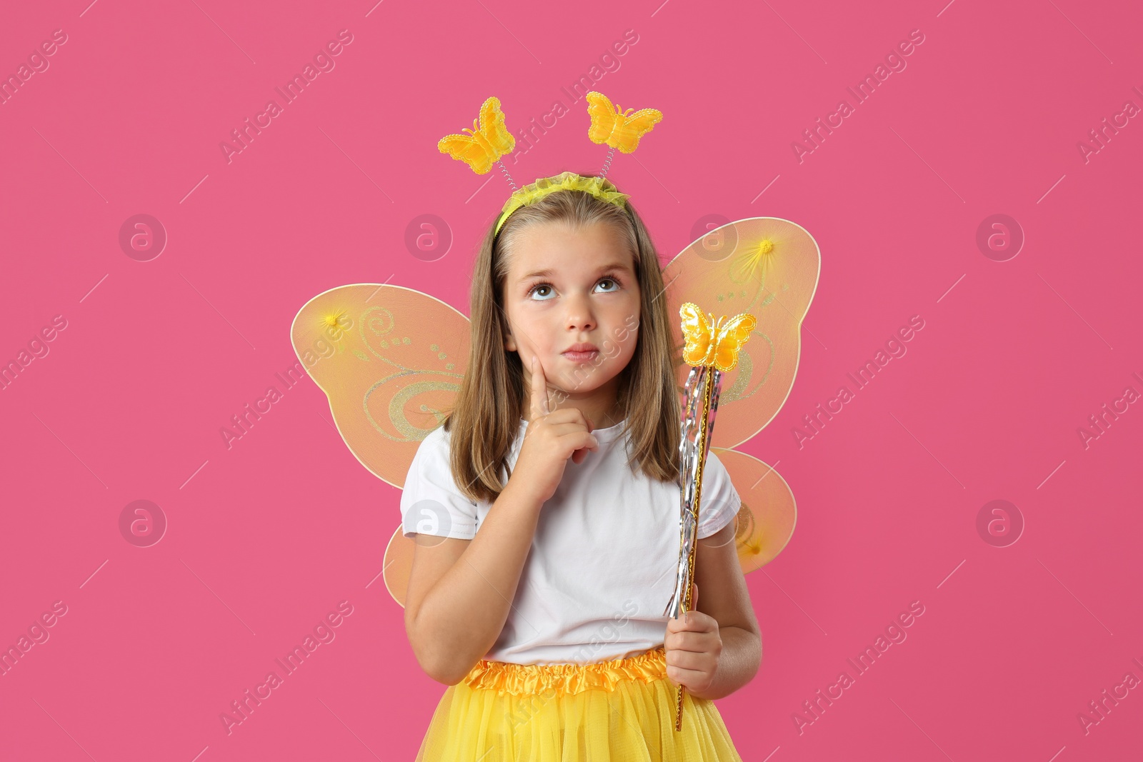 Photo of Cute little girl in fairy costume with yellow wings and magic wand on pink background