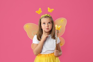 Photo of Cute little girl in fairy costume with yellow wings and magic wand on pink background