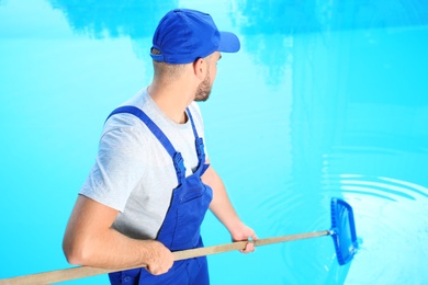 Male worker cleaning outdoor pool with scoop net