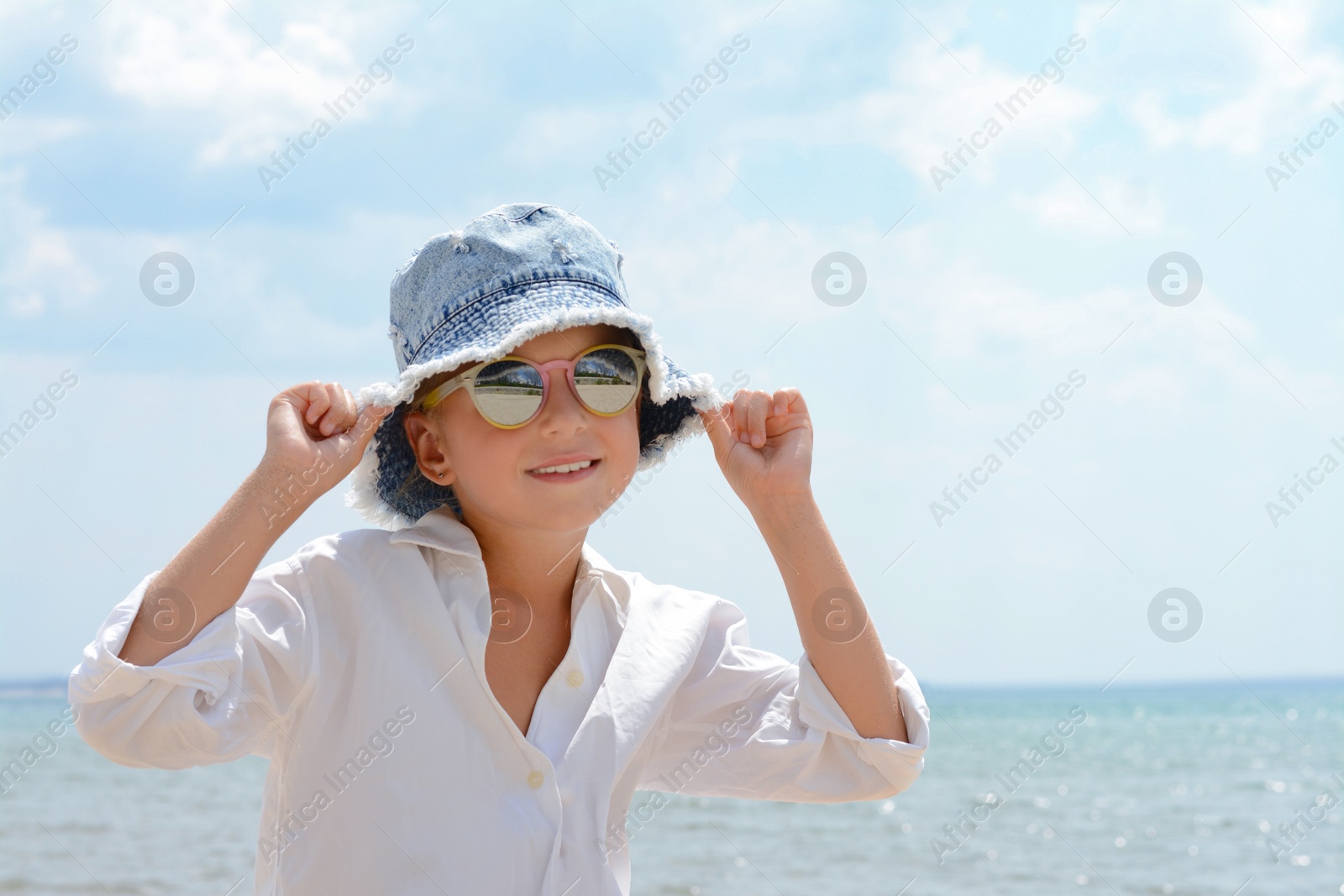 Photo of Little girl wearing sunglasses and hat at beach on sunny day. Space for text