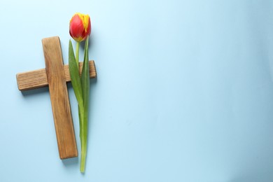 Photo of Easter - celebration of Jesus resurrection. Wooden cross and tulip on light blue background, top view. Space for text