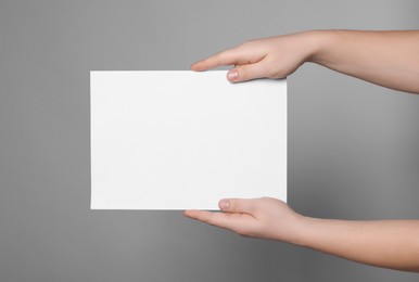 Woman holding sheet of paper on grey background, closeup. Mockup for design