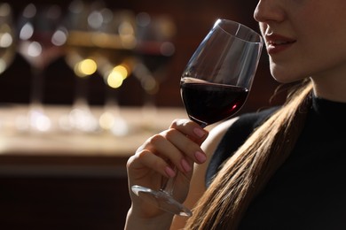 Woman with glass of red wine against blurred background, closeup. Space for text