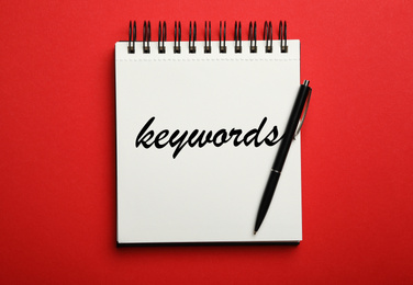 Image of Stylish notebook with text KEYWORDS and pen on red background, top view