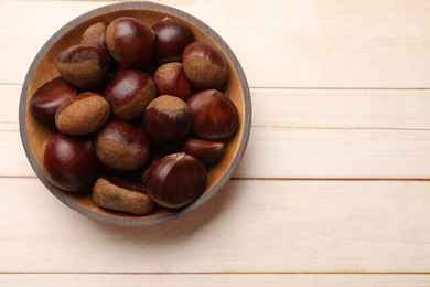 Sweet fresh edible chestnuts on light wooden table, top view. Space for text
