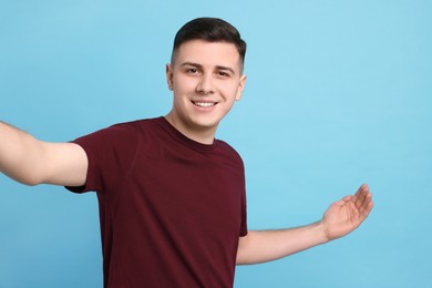 Handsome man inviting to come in against light blue background