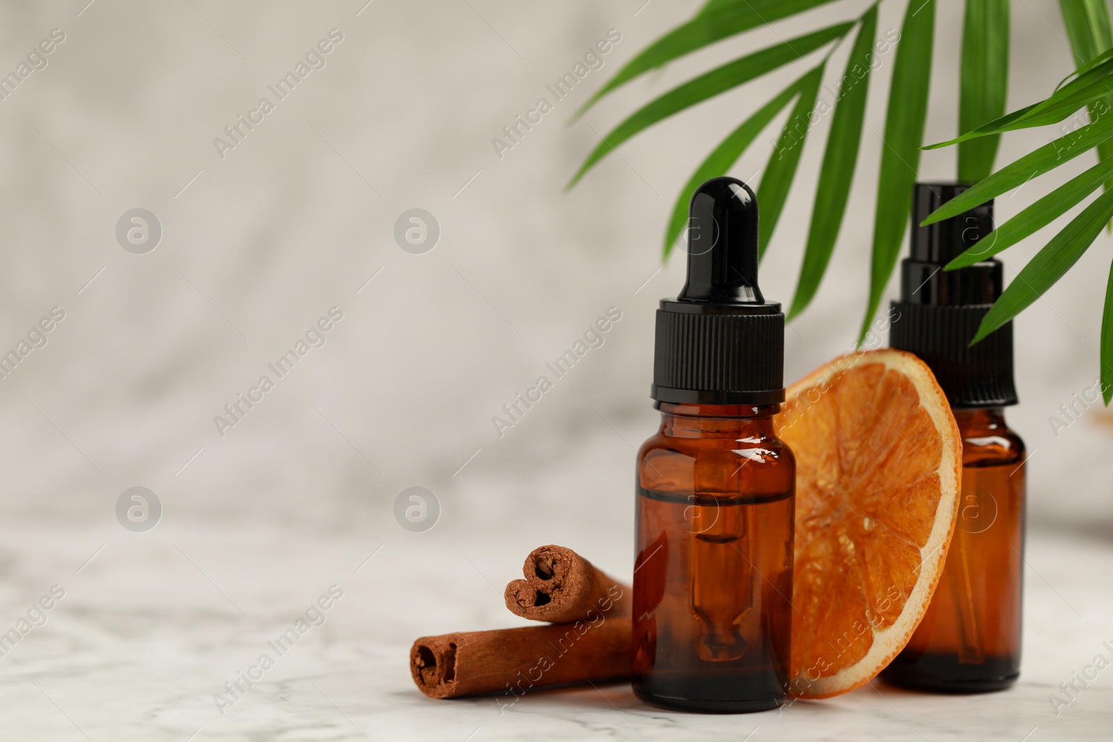 Photo of Bottles of organic cosmetic products, cinnamon sticks, dried orange slice and green leaves on light marbled background, space for text
