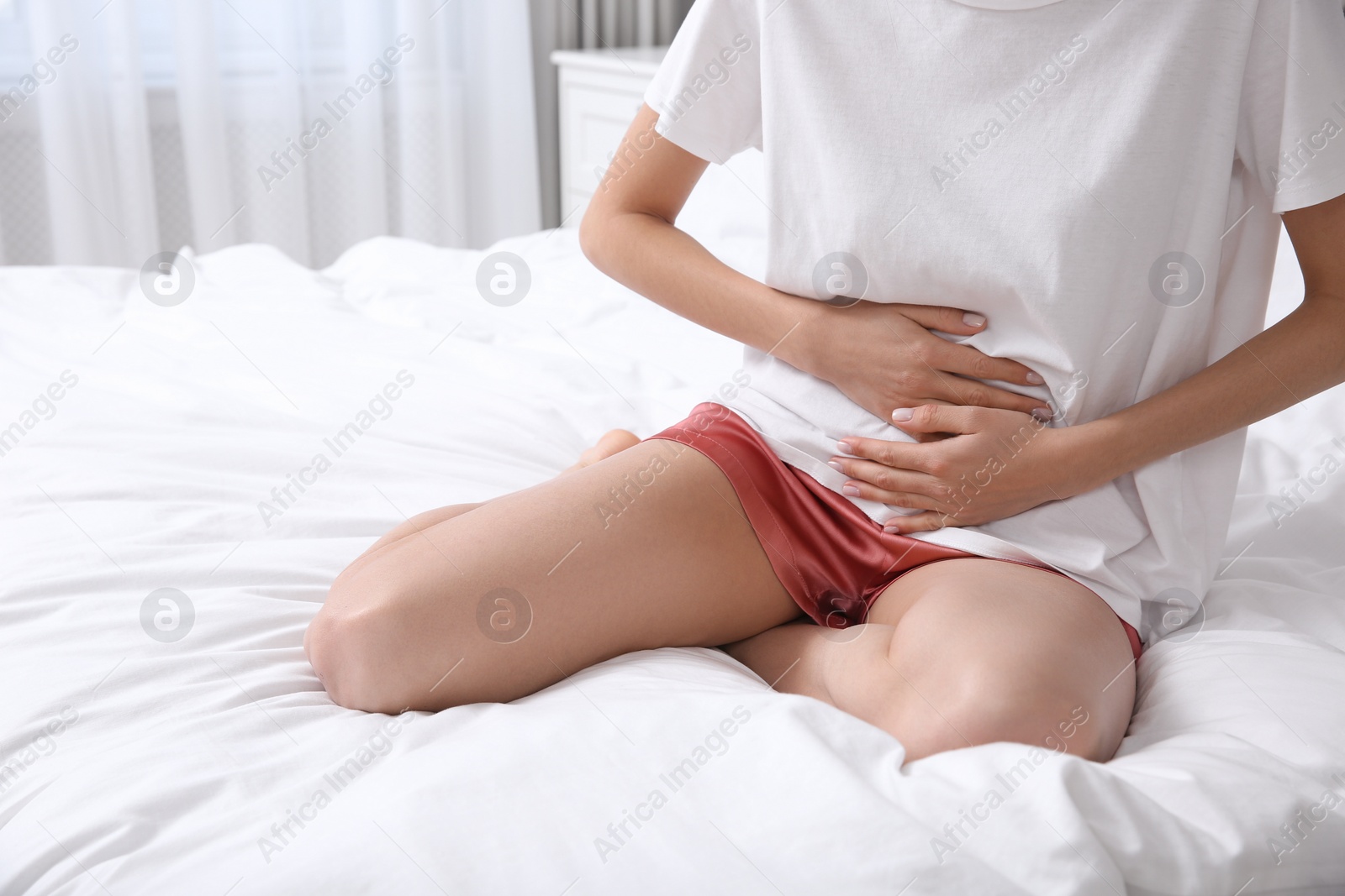 Photo of Young woman suffering from stomach ache on bed indoors, closeup