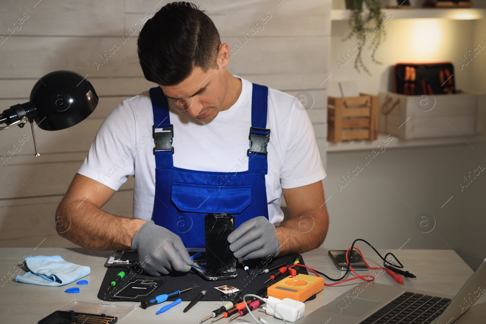 Photo of Technician repairing broken smartphone at table indoors