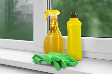 Photo of Bottles of cleaning products and rubber gloves on windowsill