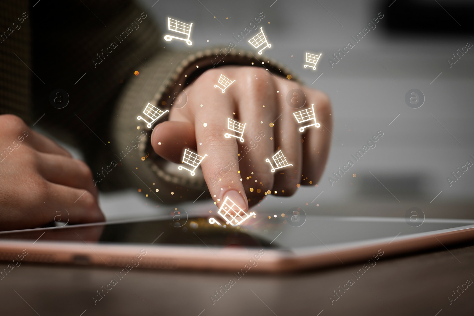 Image of Woman using tablet for online purchases at table, closeup. Shopping cart icons flying out of device screen
