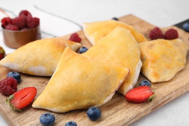 Photo of Wooden board with delicious samosas and berries on light table, closeup