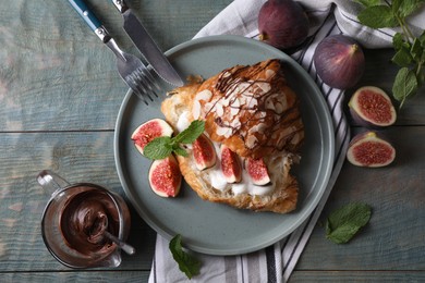 Photo of Delicious croissant with figs and cream served on light blue wooden table, flat lay