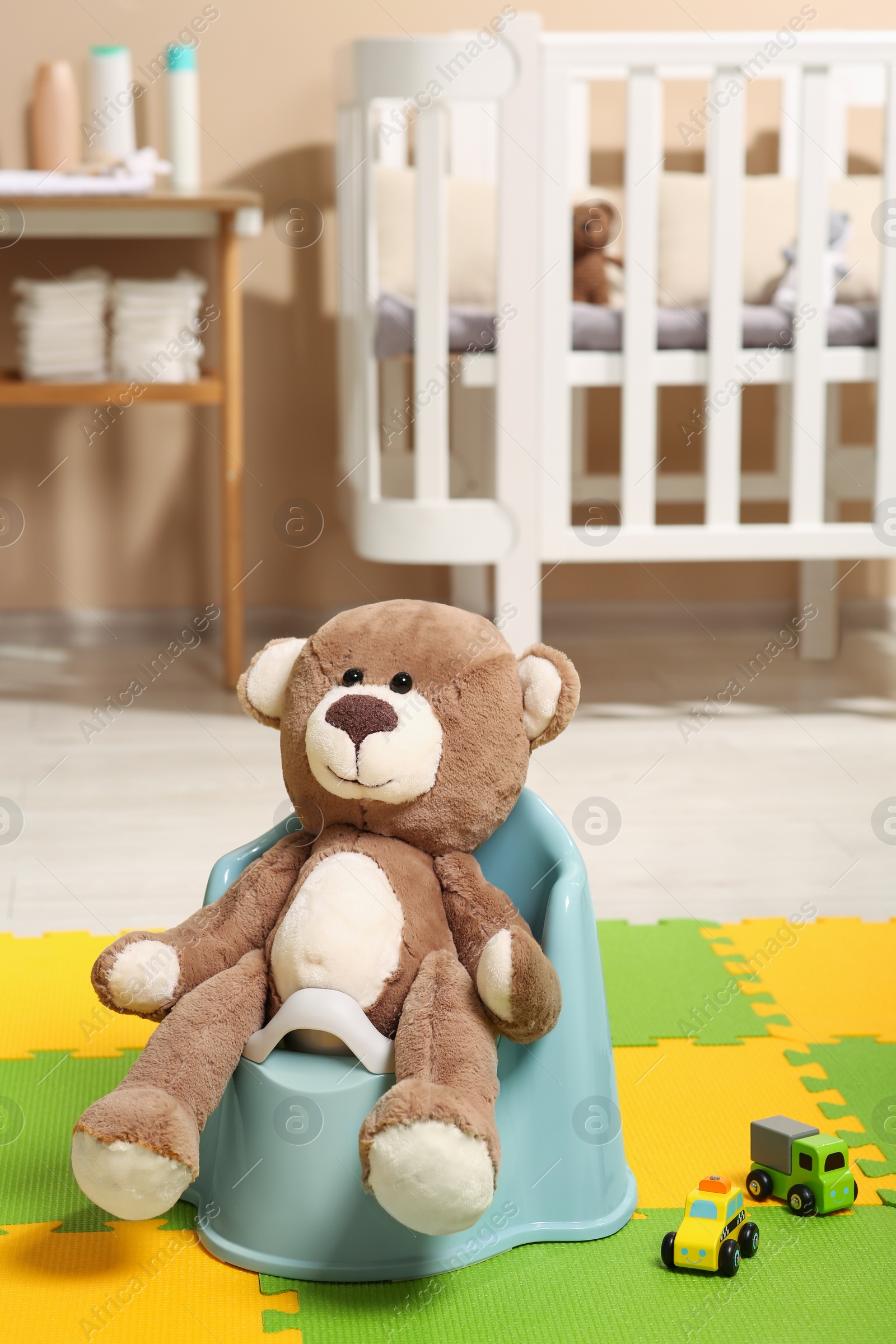 Photo of Cute teddy bear on light blue baby potty in room. Toilet training