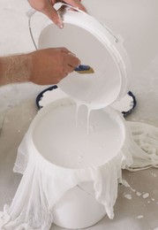 Photo of Decorator filtering paint in bucket on white floor, closeup
