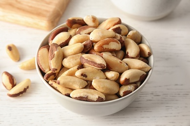 Bowl with tasty Brazil nuts on white table