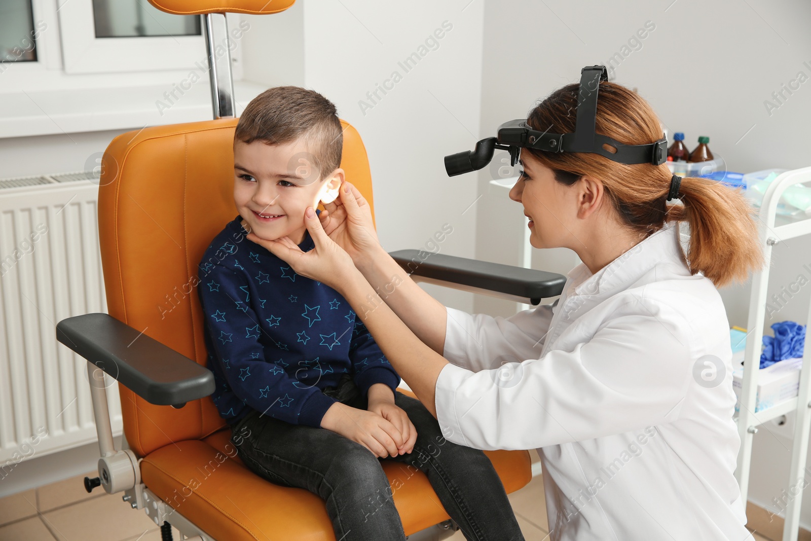 Photo of Professional otolaryngologist examining little boy in clinic. Hearing disorder