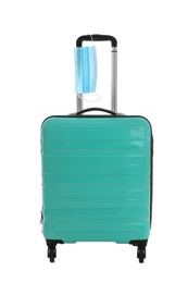 Photo of Stylish turquoise suitcase and protective mask on white background. Travelling during coronavirus pandemic