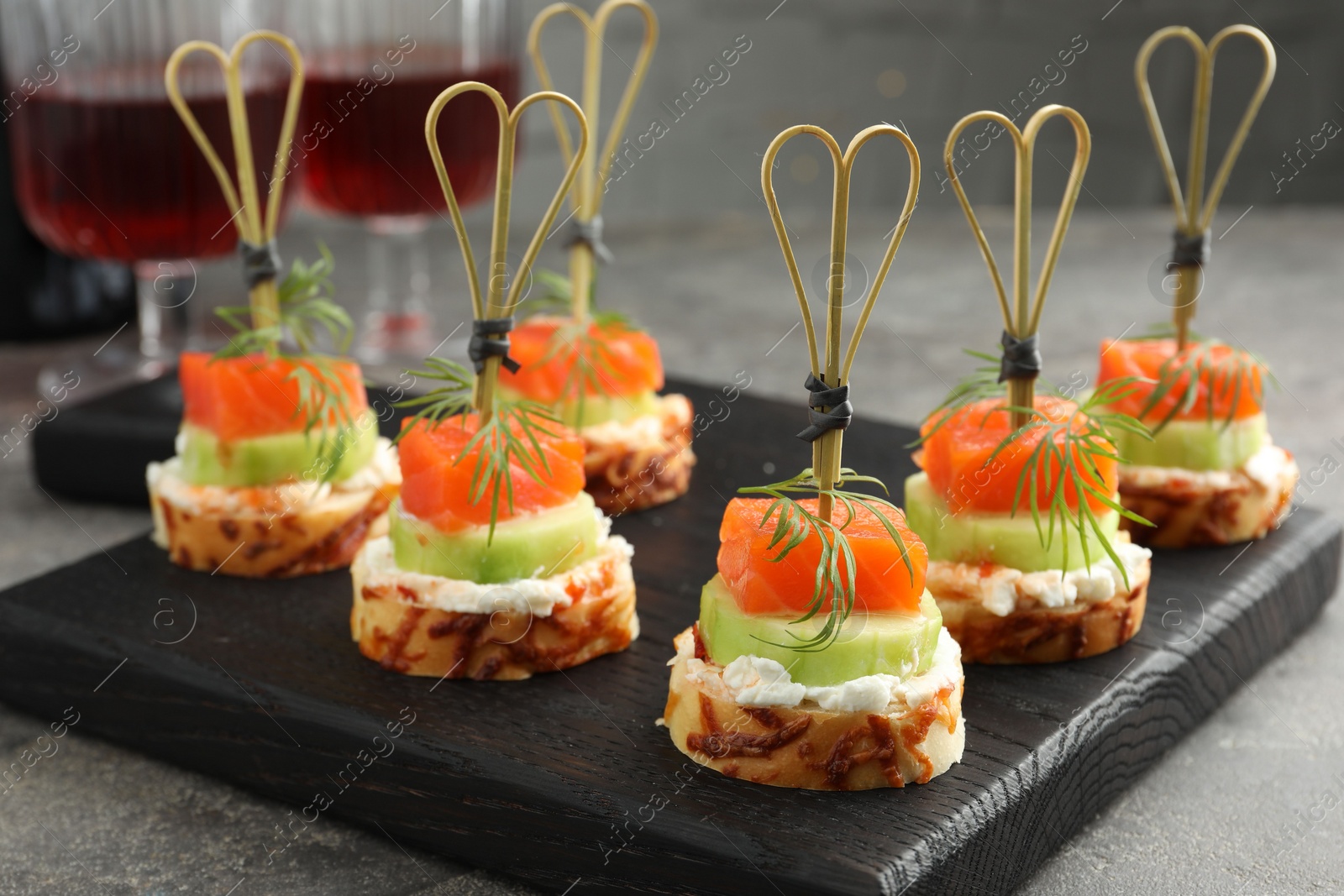 Photo of Tasty canapes with salmon, cucumber, bread and cream cheese on grey table, closeup