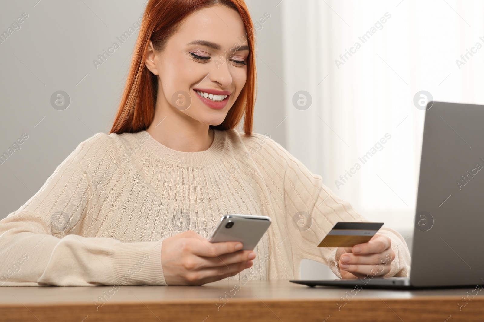 Photo of Happy woman with credit card using smartphone for online shopping at wooden table indoors