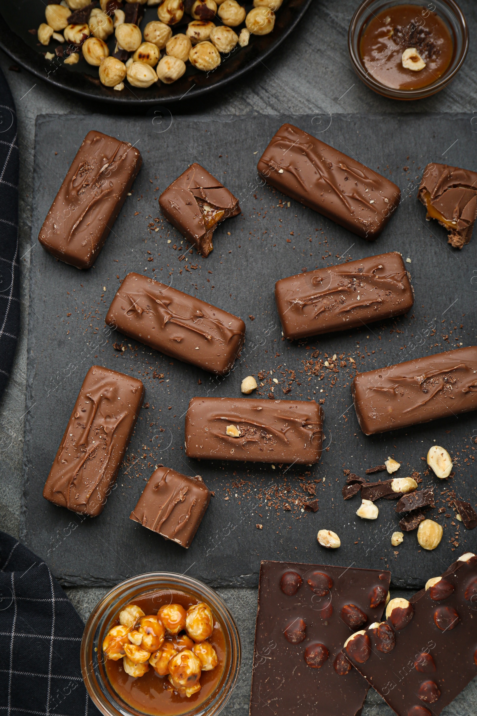 Photo of Delicious chocolate candy bars with caramel and nuts on grey table, flat lay