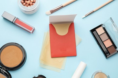 Flat lay composition with facial oil blotting tissues and makeup products on light blue background. Mattifying wipes