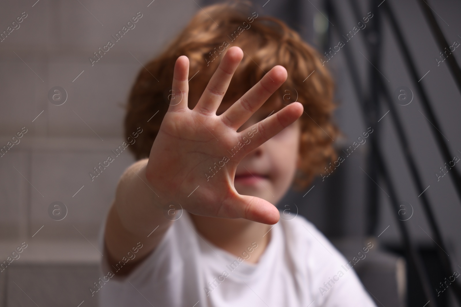 Photo of Child abuse. Boy making stop gesture sitting on stairs, selective focus