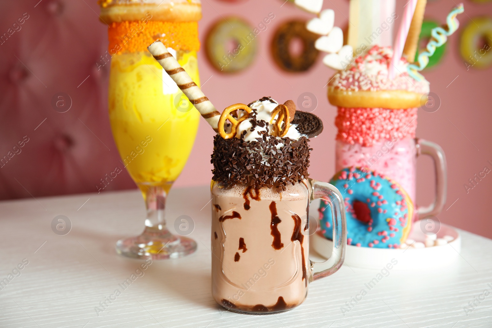 Photo of Tasty milk shakes with sweets in glassware on table at cafe