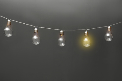 Image of Idea concept. Garland of light bulbs with one glowing on grey background 