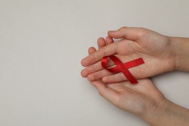 Photo of Little girl holding red ribbon on beige background, top view with space for text. AIDS disease awareness