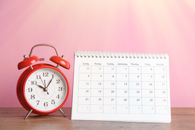 Image of Calendar and alarm clock on wooden table against pink background