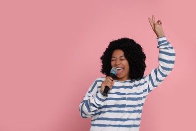 Beautiful woman with microphone singing on pink background, space for text