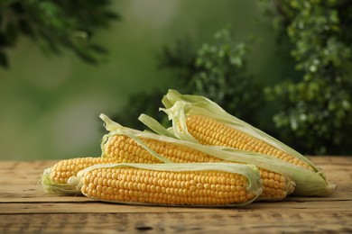 Photo of Ripe raw corn cobs on wooden table against blurred background