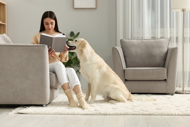 Woman reading book with cute Labrador Retriever dog at home. Adorable pet