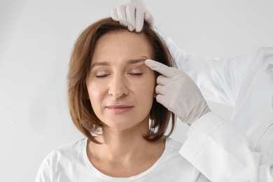 Photo of Doctor examining mature woman face before cosmetic surgery on white background