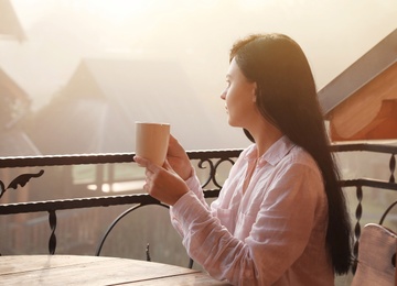 Young woman sitting at table on balcony with cup of tea in morning