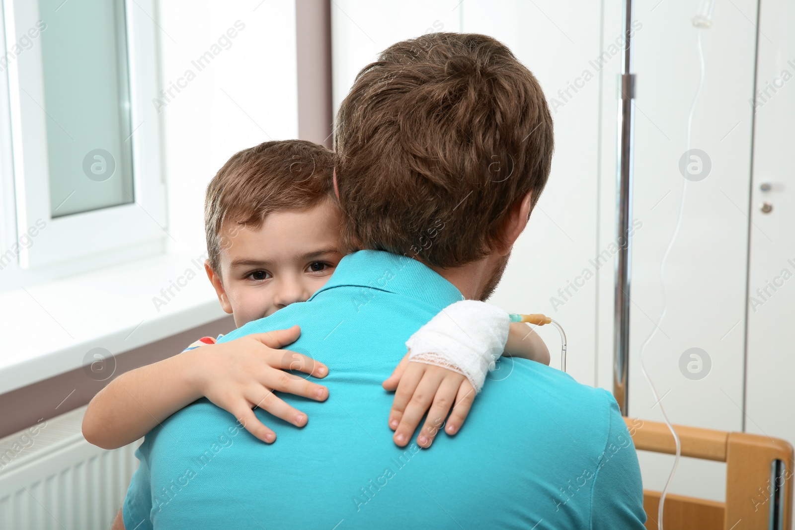 Photo of Little child with intravenous drip hugging his father in hospital