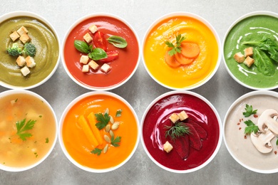 Various cream soups in bowls on grey background, top view