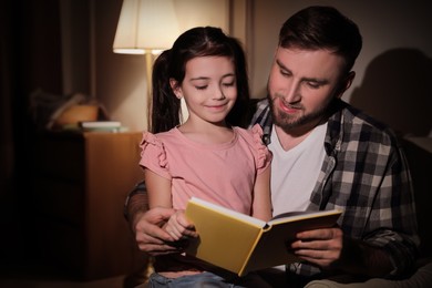 Photo of Little girl with father reading fairy tale at home in evening