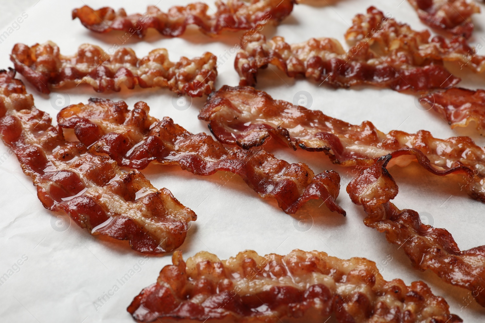 Photo of Slices of tasty fried bacon on white table, closeup