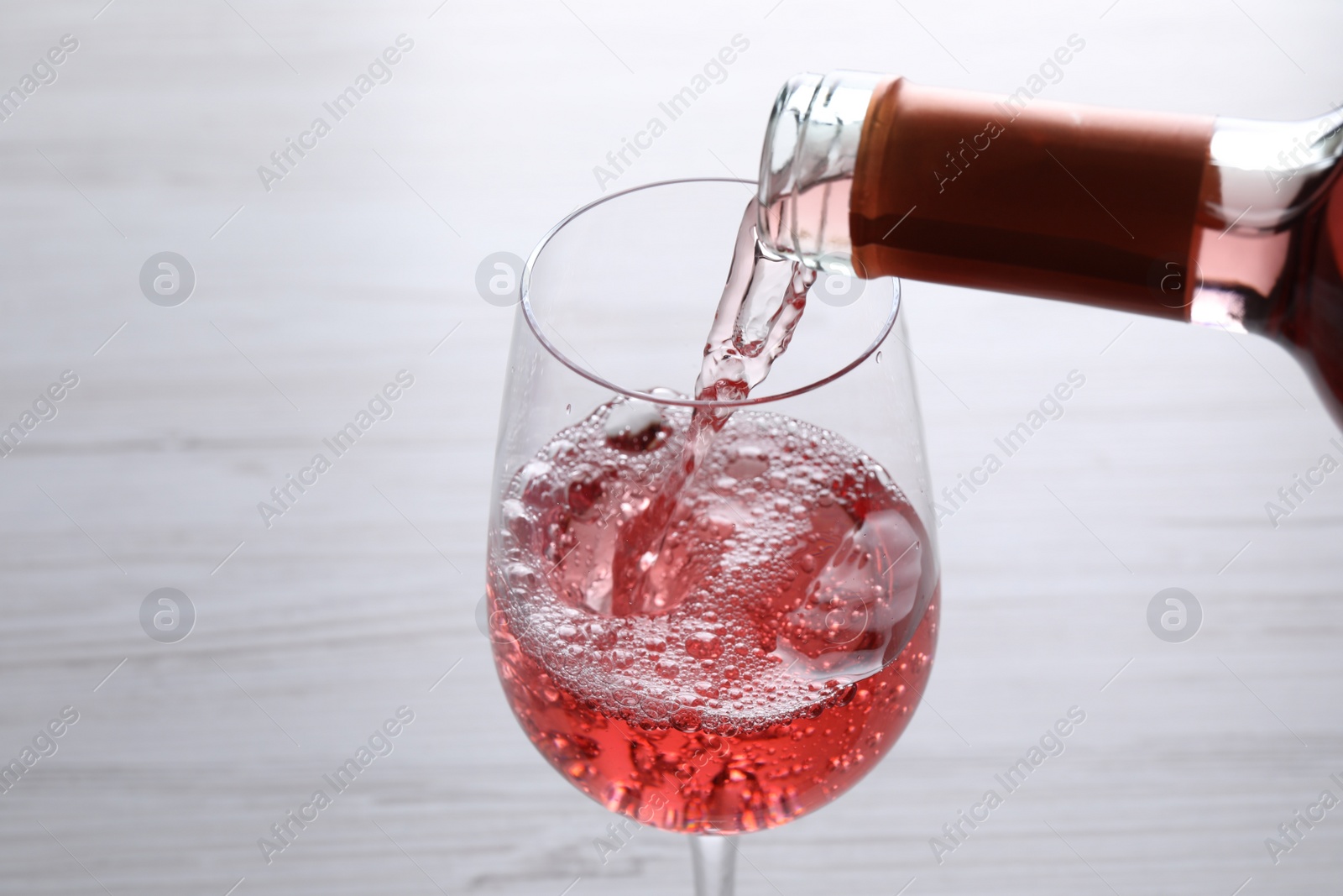 Photo of Pouring delicious rose wine into glass on white table, closeup