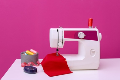 Photo of Modern sewing machine on table against color background