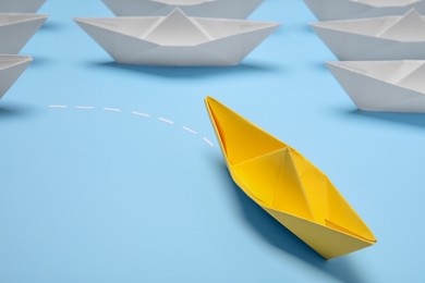 Photo of Yellow paper boat floating away from others on light blue background, closeup with space for text. Uniqueness concept
