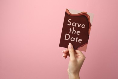 Photo of Woman holding beautiful card with Save the Date phrase on pink background, closeup. Space for text