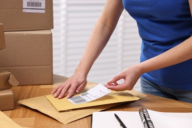 Parcel packing. Post office worker sticking barcode on bag at wooden table indoors, closeup