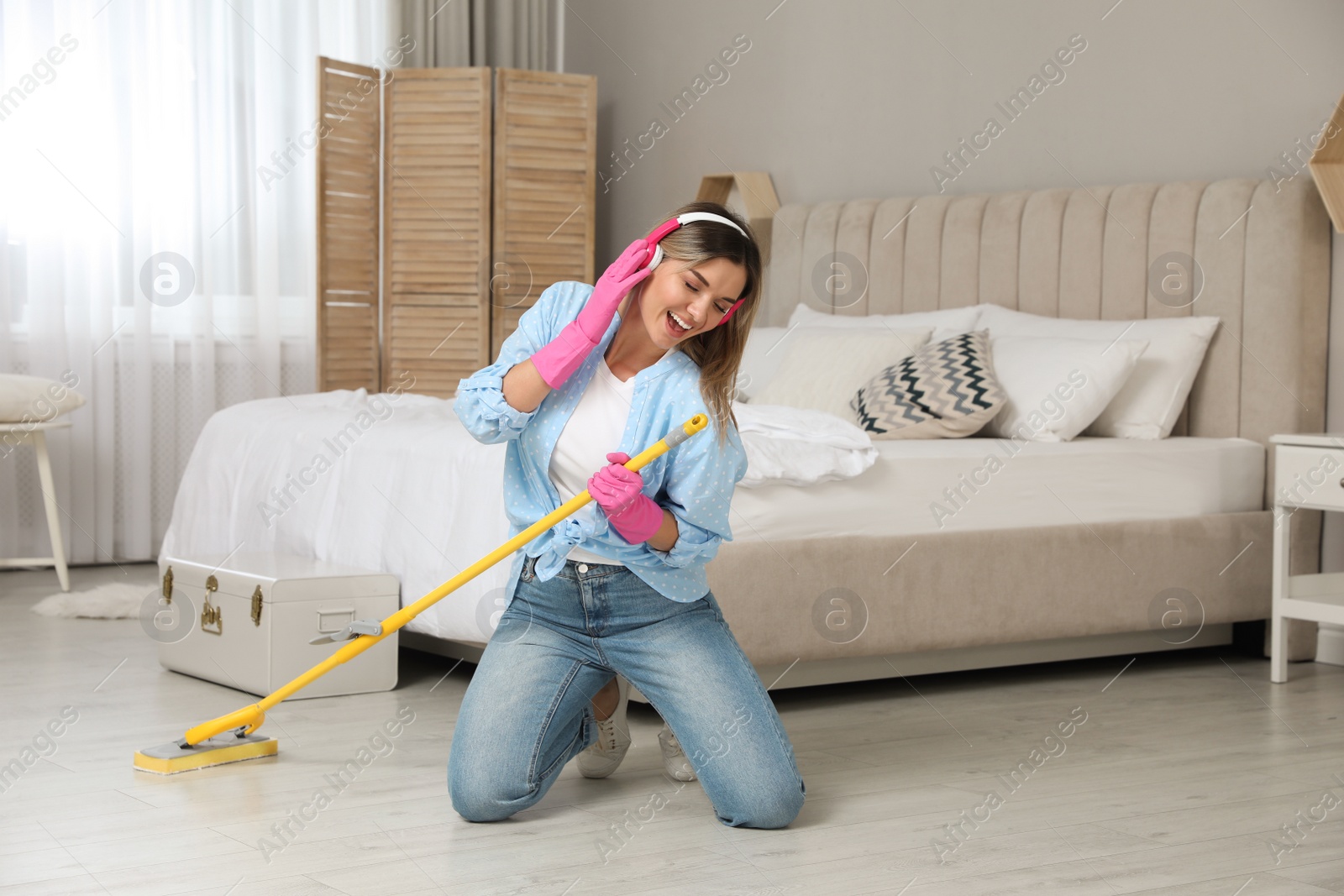 Photo of Woman in headphones with mop singing while cleaning at home